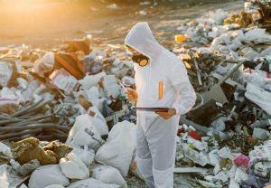 Un expert en combinaison de protection analyse des déchets sur un site d’enfouissement dans le cadre d’un projet de valorisation énergétique.