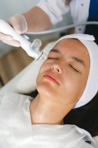 Femme allongée recevant un soin du visage avec un appareil esthétique, illustrant l’excellence et l’innovation au service du bien-être chez Aunessa.