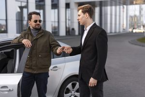 Deux hommes échangent des clés à côté d’une voiture après une vente.