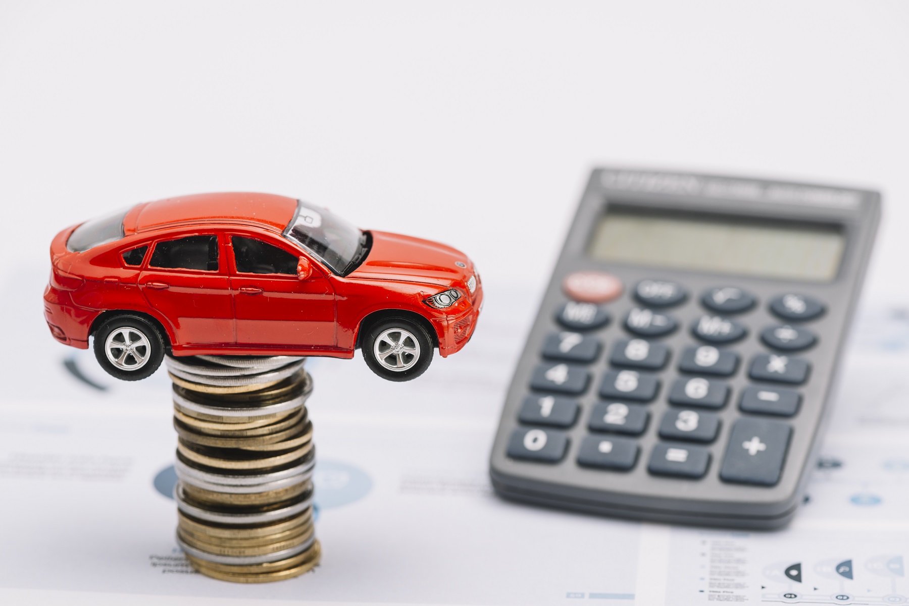 Voiture-jouet posée sur une pile de pièces de monnaie, à côté d'une calculatrice