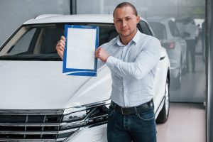 Un homme debout devant une voiture blanche moderne, tenant un papier à la main.