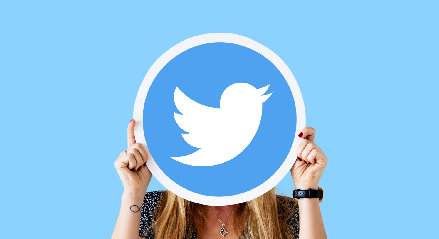 Une femme aux cheveux longs cache son visage derrière un panneau circulaire affichant le logo de Twitter sur un fond bleu clair.