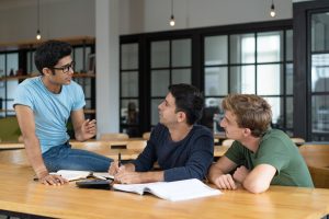 Trois jeunes hommes discutent ensemble autour d’une table avec des livres et des cahiers