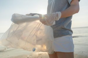 Homme au bord de la mer tenant un sac rempli de bouteilles en plastique.