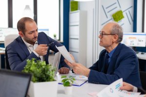 Un entrepreneur senior discute avec un collègue lors d’une conférence, tenant des documents en main