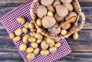 Pommes de terre pelées avec éplucheur de pommes de terre dans un panier et sur un tissu de pique-nique, sur une table en bois gris