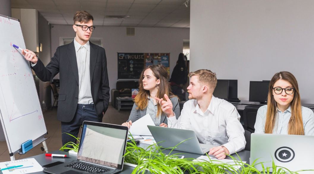Équipe en réunion stratégique dans un bureau moderne, un manager présente un graphique sur un tableau blanc