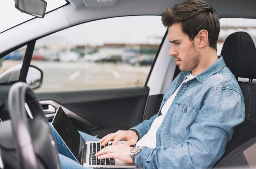 Homme assis dans une voiture en train de travailler sur un ordinateur portable