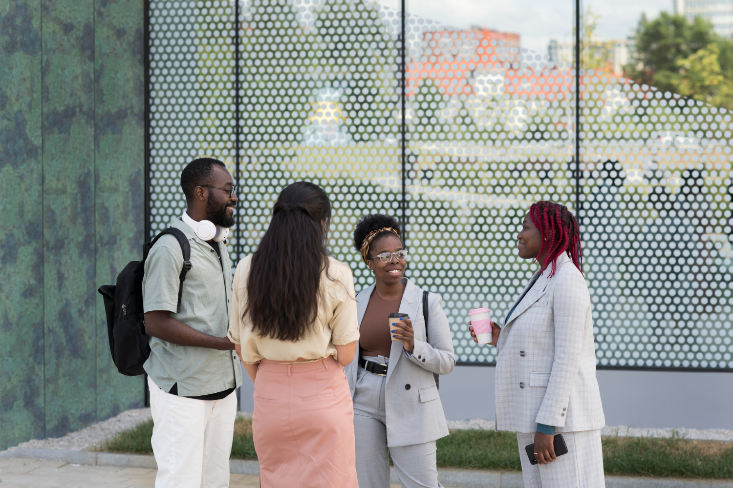 Un groupe de quatre jeunes étudiants discutant en extérieur devant une façade moderne en verre.
