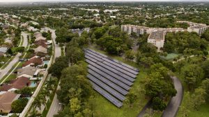 Vue aérienne d’un quartier résidentiel avec des maisons, des immeubles et un grand champ de panneaux solaires installé sur une zone verte entourée d’arbres