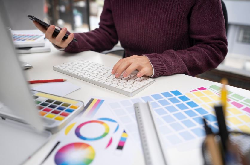 Personne travaillant sur un ordinateur avec des échantillons de couleurs et des outils de design sur le bureau