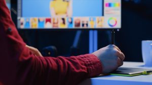 Graphiste travaillant sur une tablette graphique devant un écran rempli de visuels colorés