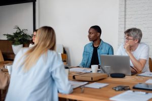 Une équipe multiculturelle collabore lors d'une réunion de travail autour d'une grande table en bois dans un bureau moderne et lumineux.