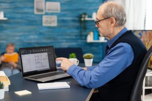 Expert senior analysant des plans d'architecte sur laptop