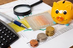 Une tirelire en forme de cochon jaune posée sur des graphiques financiers, à côté de piles de pièces de monnaie, d'une calculatrice et d'un stylo