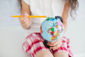 Un enfant assis tient un petit globe terrestre coloré d'une main et pointe le sommet avec un crayon jaune de l'autre.