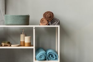 Une étagère de salle de bain blanche et bois présentant des serviettes de toilette roulées aux couleurs terreuses et bleues