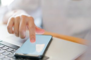 une personne utilisant son index pour naviguer sur l'écran d'un smartphone posé sur un ordinateur portable