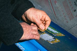 une personne âgée en train de gratter un ticket de jeu de grattage à l'aide d'une pièce de monnaie.