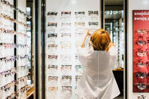 Une opticienne vue de dos en train de ranger une paire de lunettes sur un présentoir mural.
