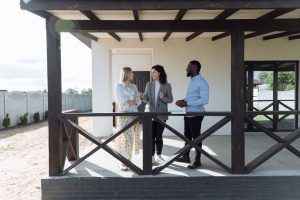 Une conseillère échangeant avec un couple sur la terrasse couverte d'une maison moderne.