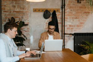 Deux hommes travaillent sur leurs ordinateurs portables autour d'une grande table en bois dans un café ou espace de coworking