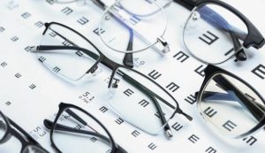 Plusieurs paires de lunettes de vue aux montures variées sont disposées sur une échelle d'acuité visuelle comportant des lettres et des symboles de test optométrique.
