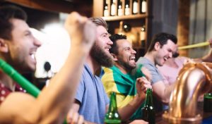 Des supporters enthousiastes crient de joie au comptoir d'un bar en regardant un match, bouteilles de bière à la main