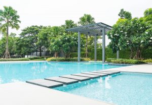 Une vaste piscine extérieure aux eaux turquoise est traversée par des dalles de pas japonais